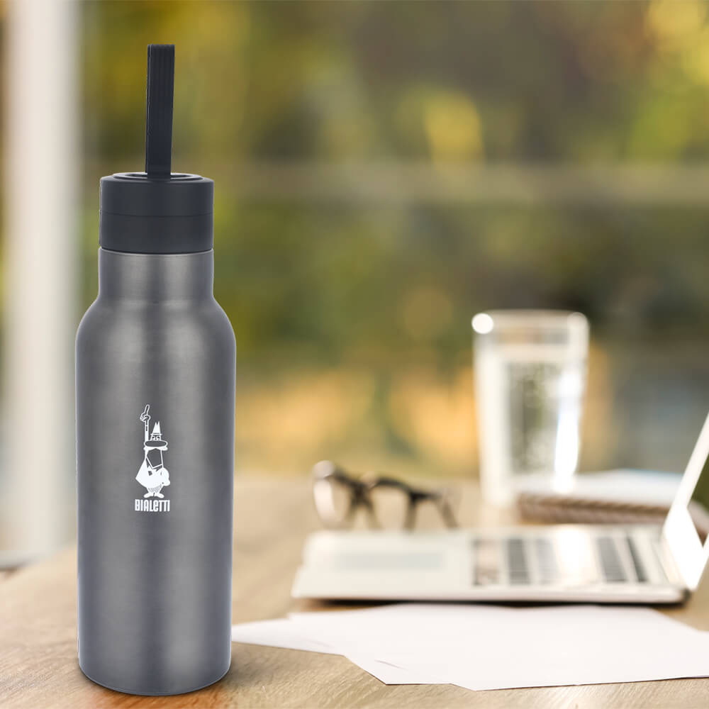 Bialetti grey thermal drinks bottle on table with laptop and glass of water